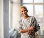 Charismatic African American man with books, smiling in a sunlit apartment.
